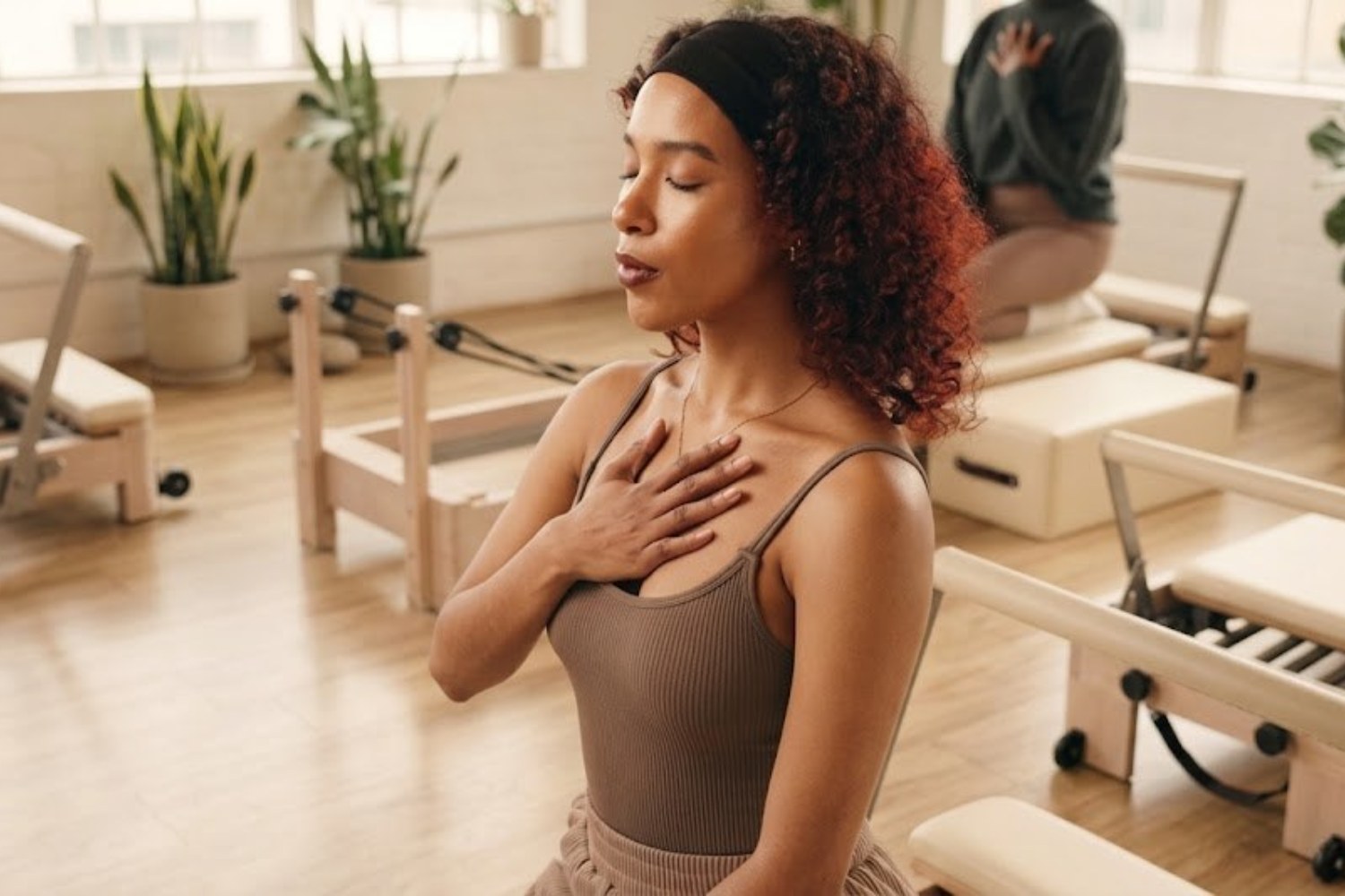 Mulher de olhos fechados com a mão sobre o peito, respirando conscientemente em um estúdio de Pilates